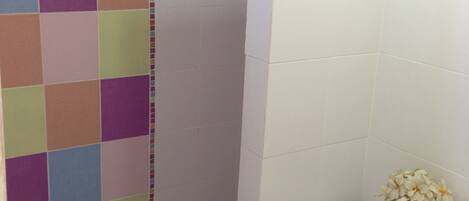 A bathroom with a shower area, a toilet, and a small plant on the toilet.