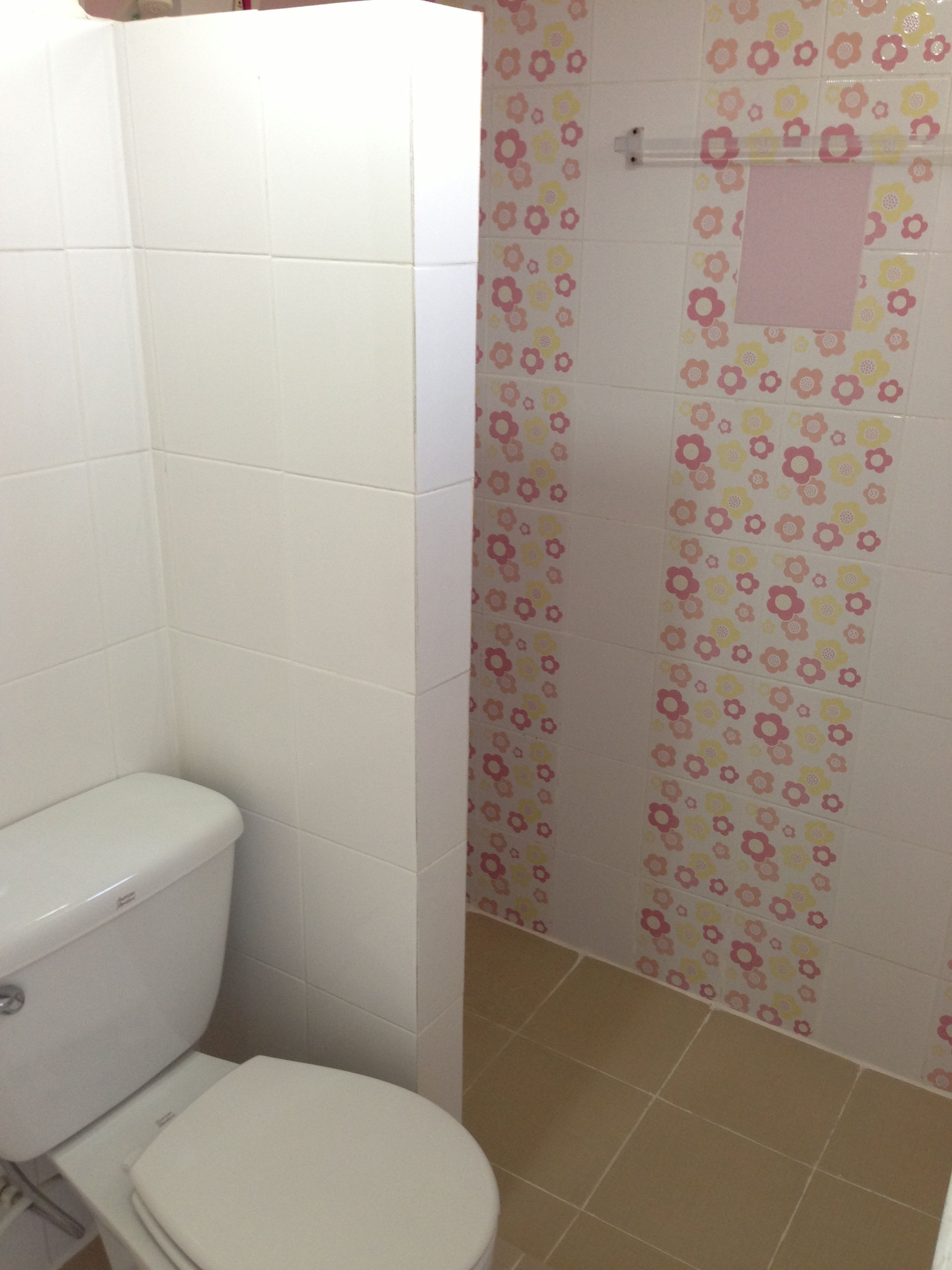 Un baño con inodoro, zona de ducha con azulejos de motivos florales y un perchero para toallas.