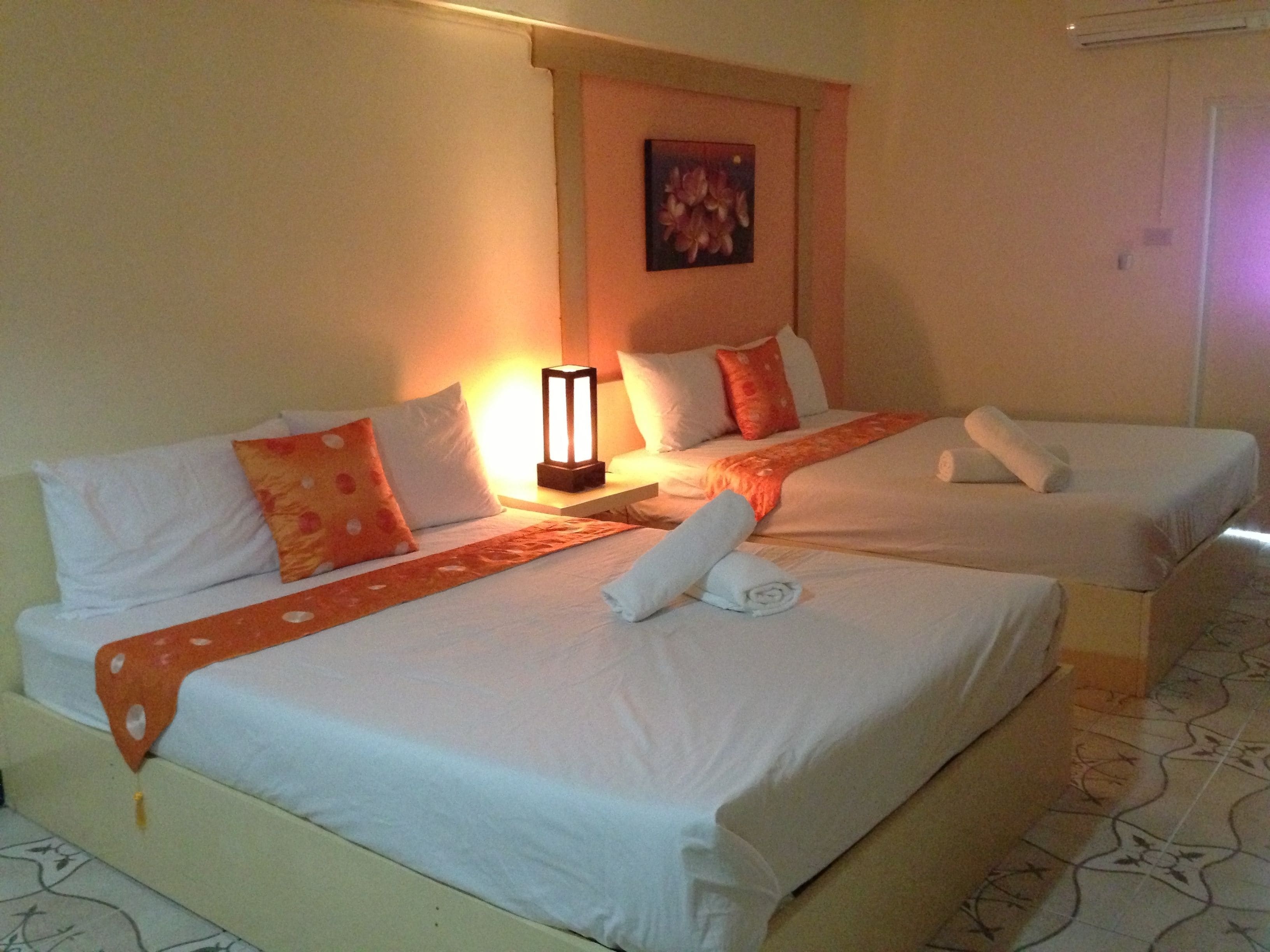Une chambre d’hôtel avec deux lits, chacun agrémenté de draps blancs et de touches de couleur orange, une table de chevet avec une lampe et un tableau encadré au mur.