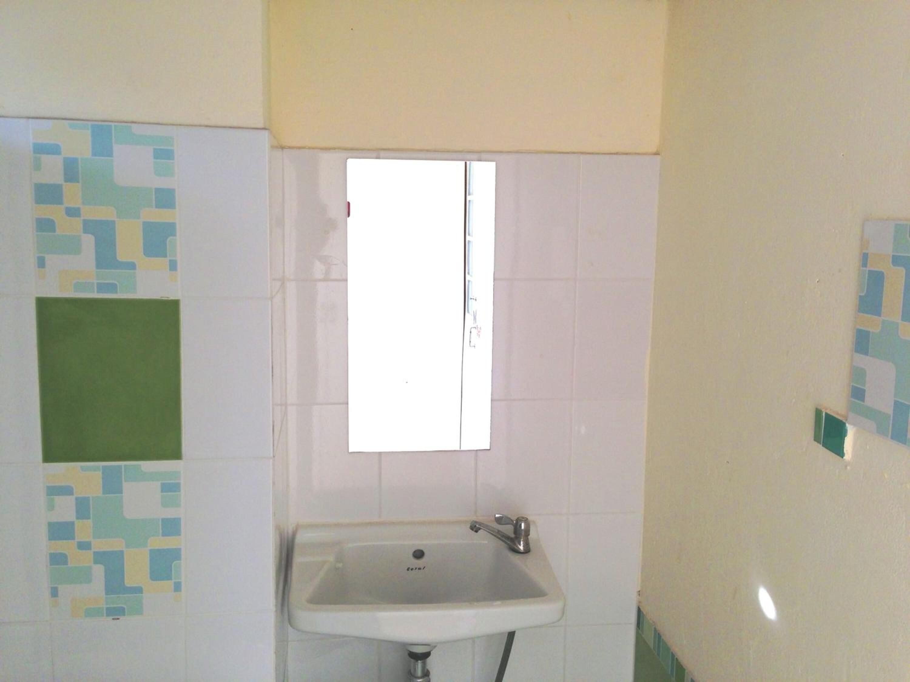 Een badkamer met een wit wastafel, een raam en betegelde muren.