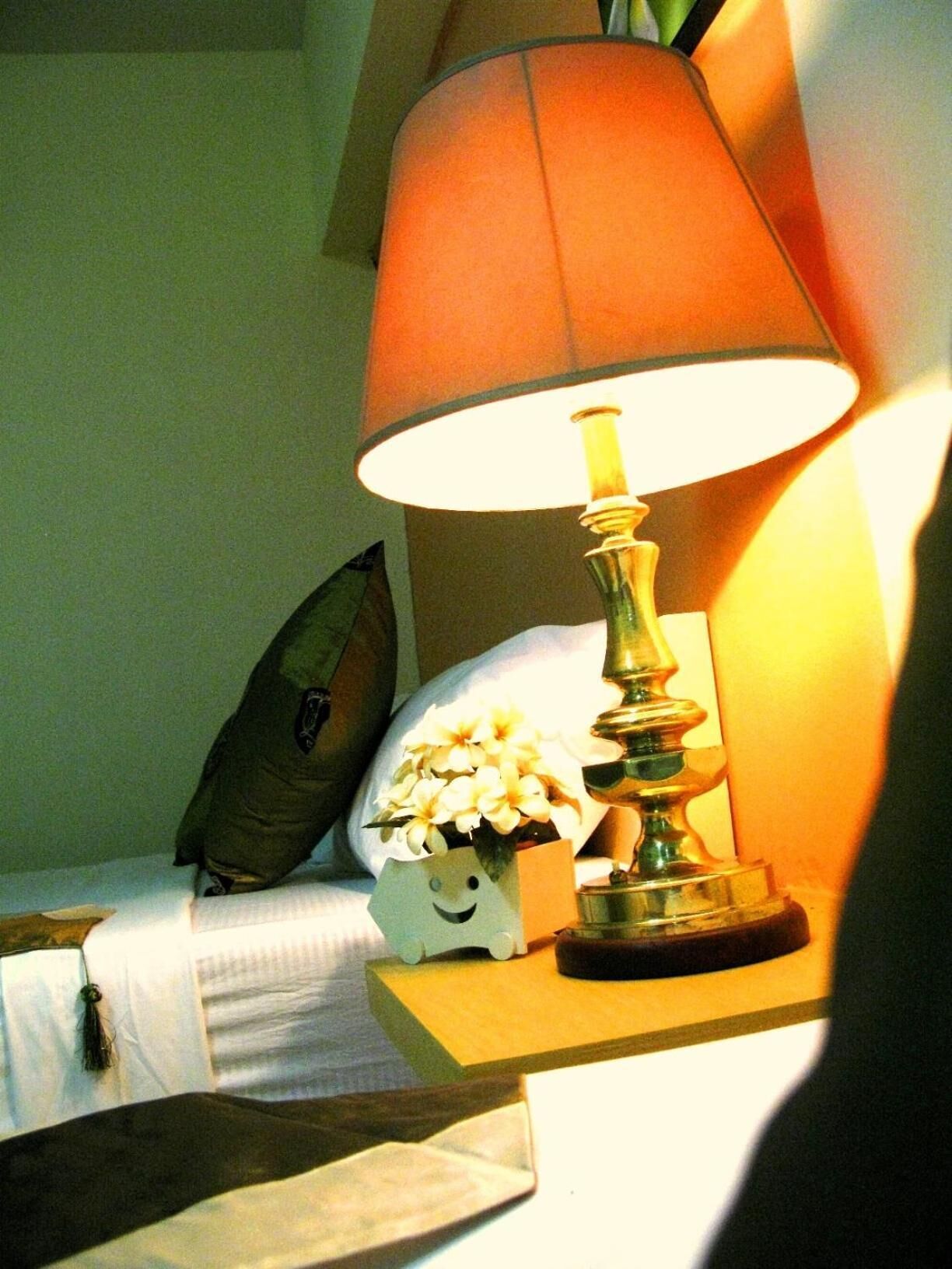 Una mesita de noche con una lámpara, un florero y un almohadón sobre la cama.