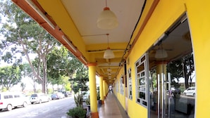 A corridor with yellow walls and a tiled floor, leading to a glass door entrance.
