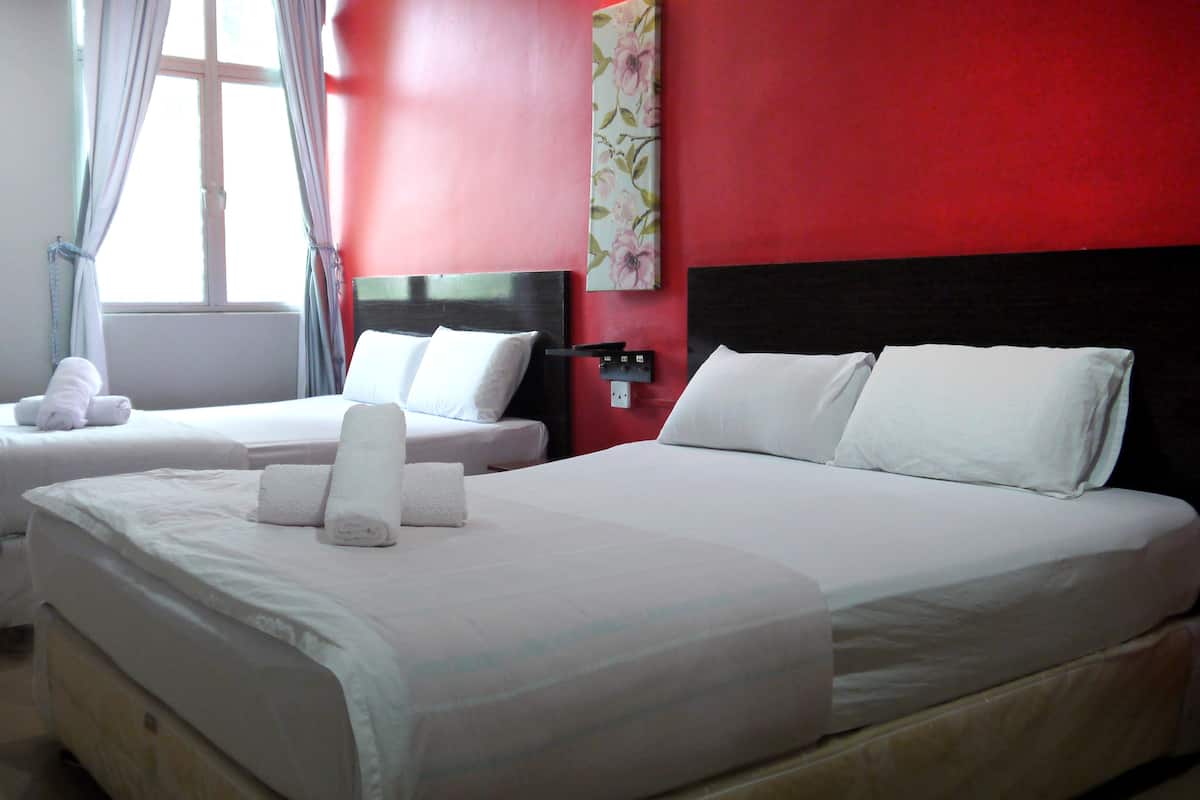 Ein Hotelzimmer mit zwei Betten, weißen Laken, einer roten Akzentwand und einem Fenster mit Vorhängen.