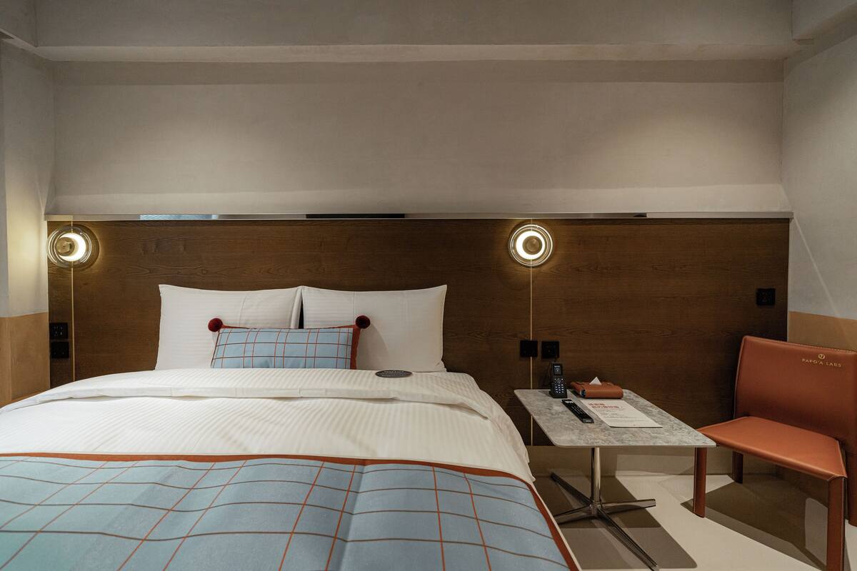 Una habitación de hotel moderna con una cama grande, una mesita con una silla y un cabecero de madera.