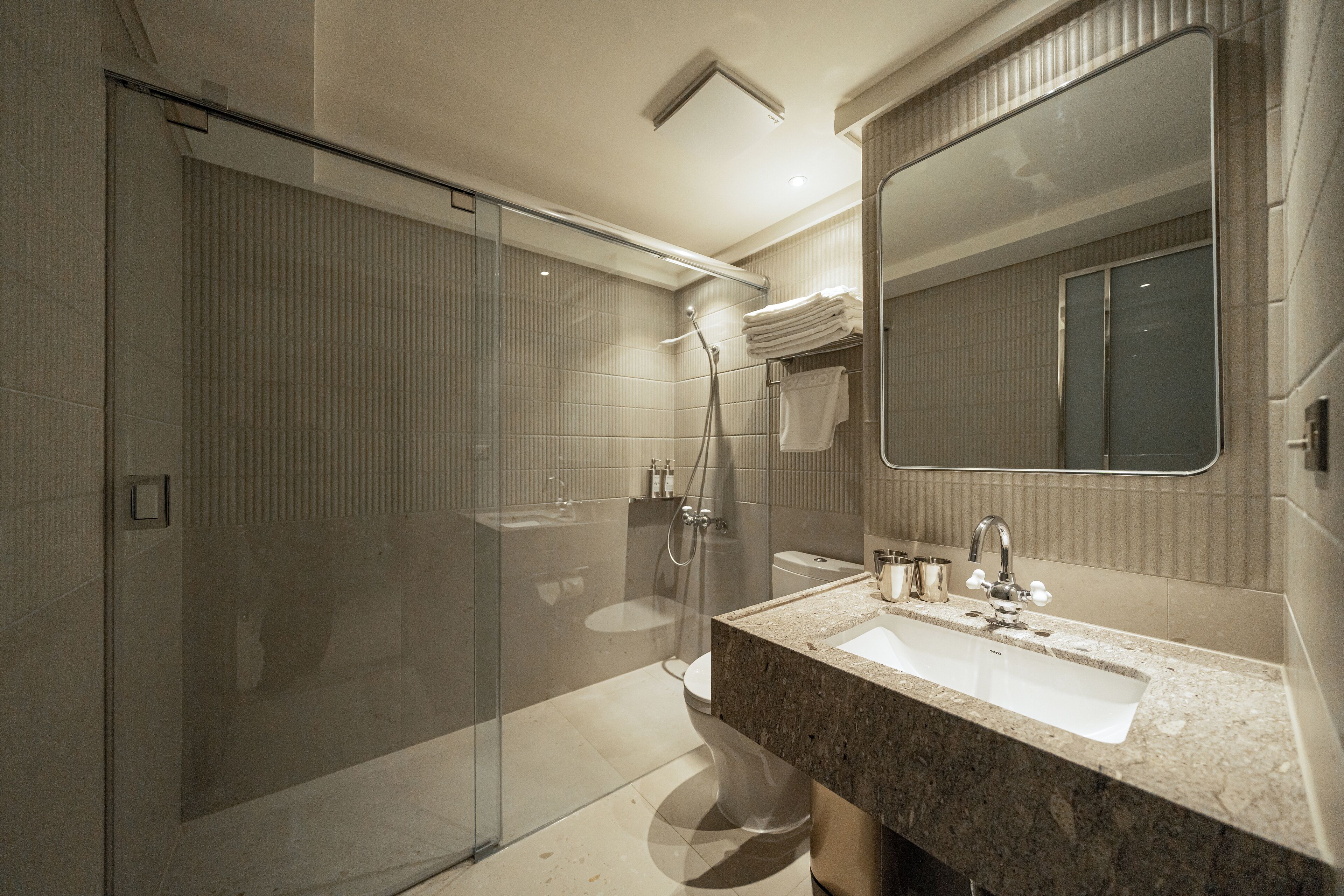 A modern bathroom with a glass shower enclosure, a sink with a marble countertop, and a large mirror above the sink.
