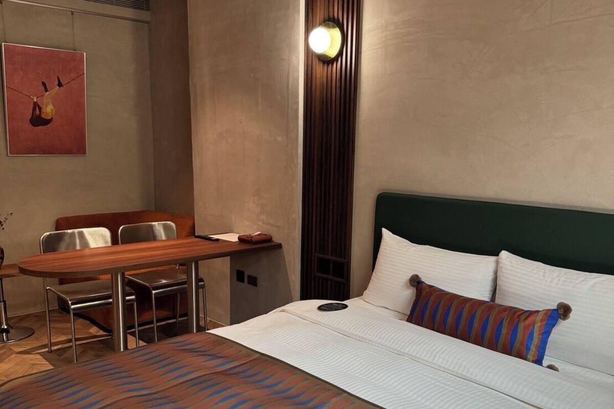 Una habitación de hotel con una cama, un escritorio, una silla y una lámpara de pared.