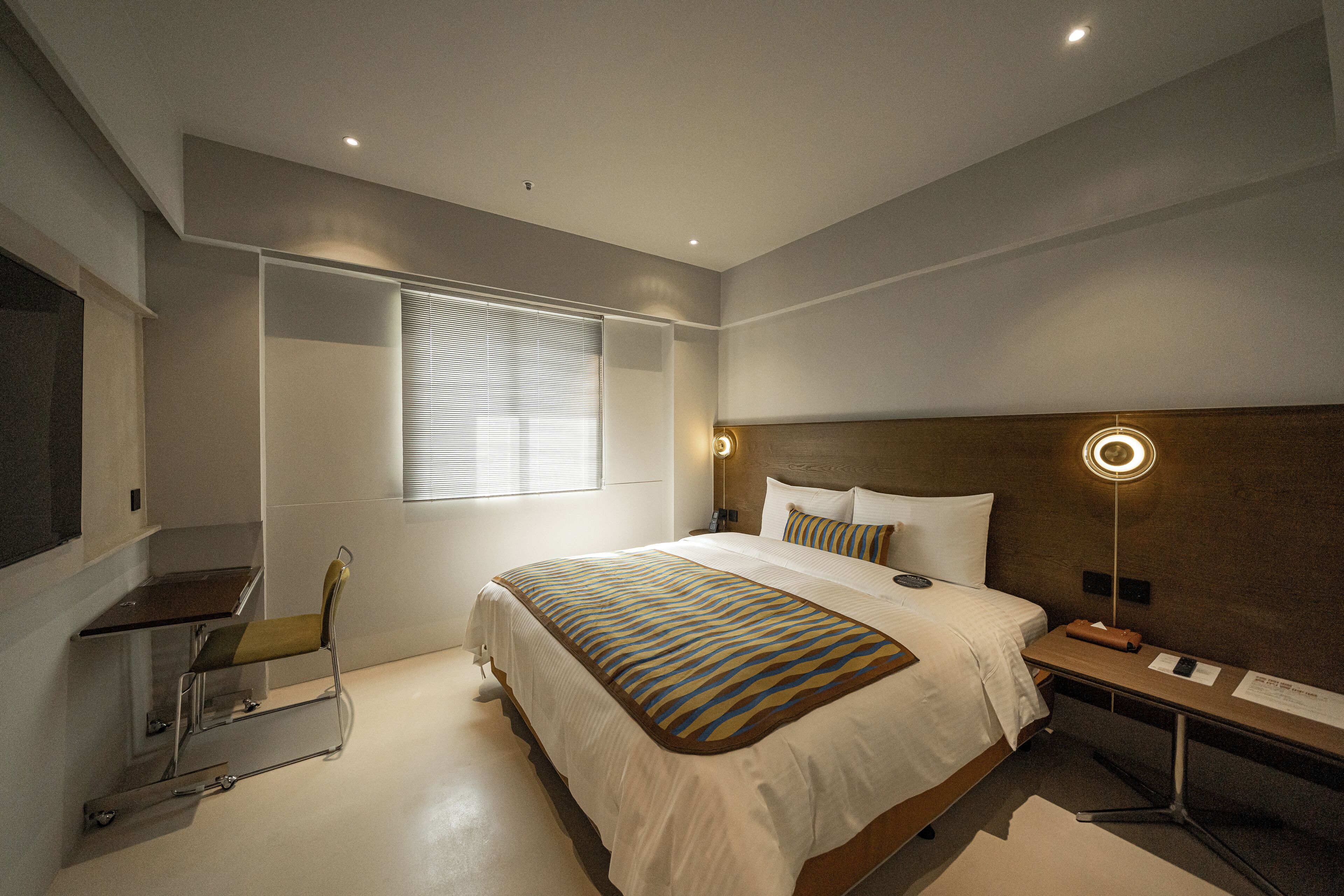 Moderni hotellihuone, jossa on suuri sänky, yöpöytä, lamppu ja tuoli.
