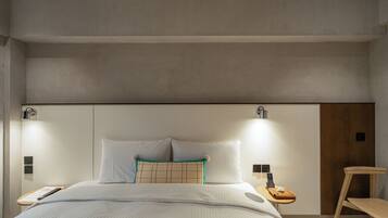 A modern hotel room with a large bed, bedside tables, a wooden chair, and a nightstand with a phone and remote control.