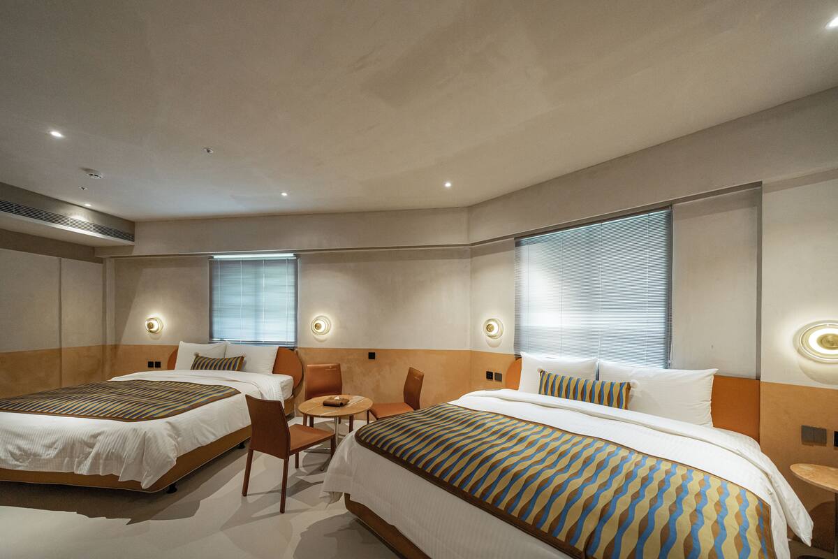 Habitación de hotel con dos camas, una mesita y una silla.