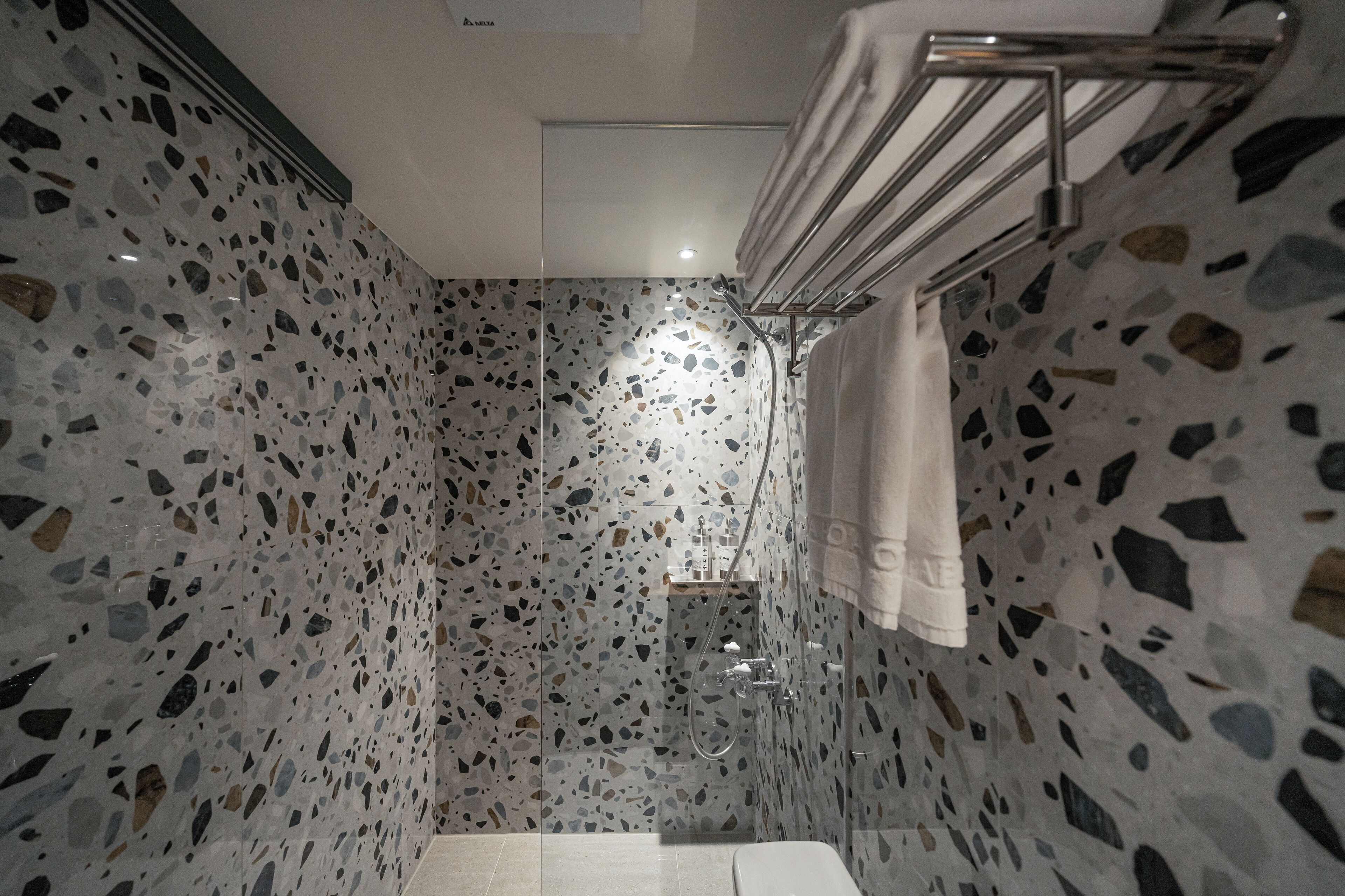 A bathroom with terrazzo flooring, a glass shower enclosure, and a towel rack.