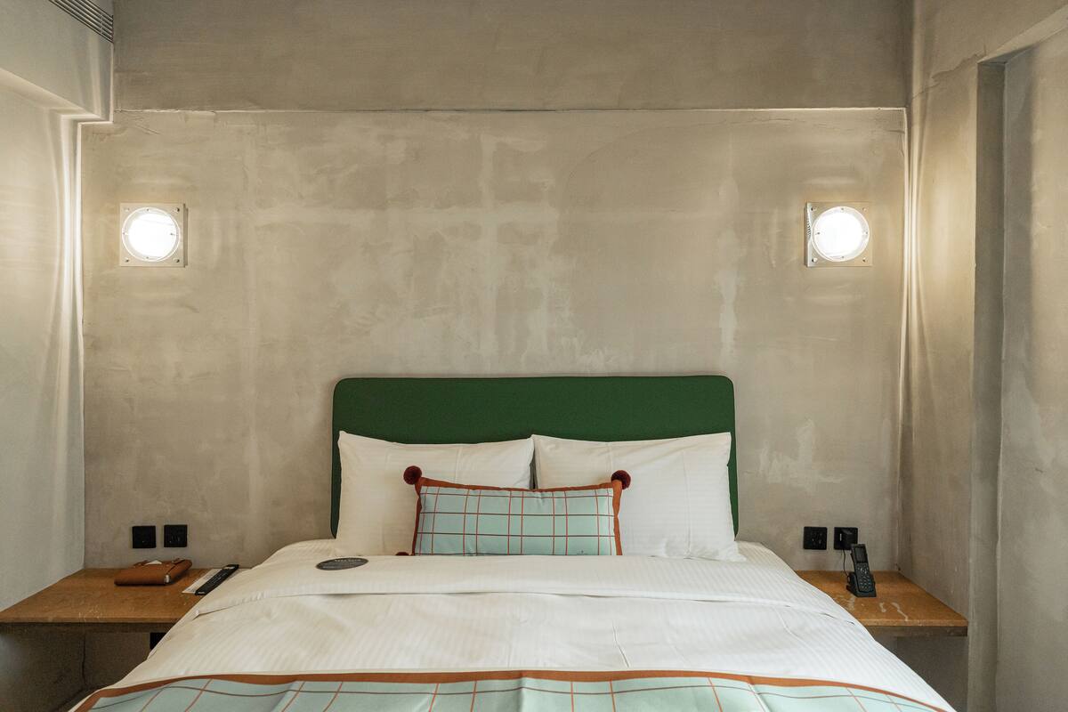 Una habitación de hotel con una cama, una mesita de noche, un teléfono y una lámpara fijada a la pared.