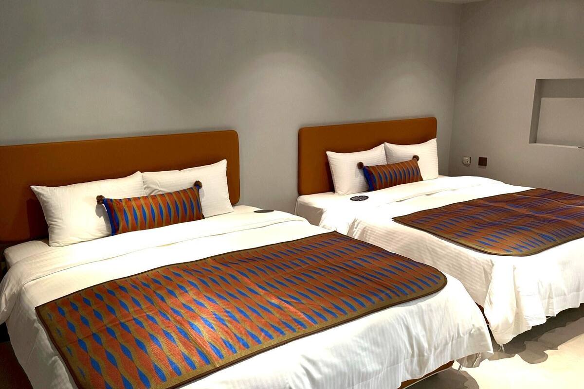 Habitación de hotel con dos camas, cada una con una colcha y almohadas estampadas.