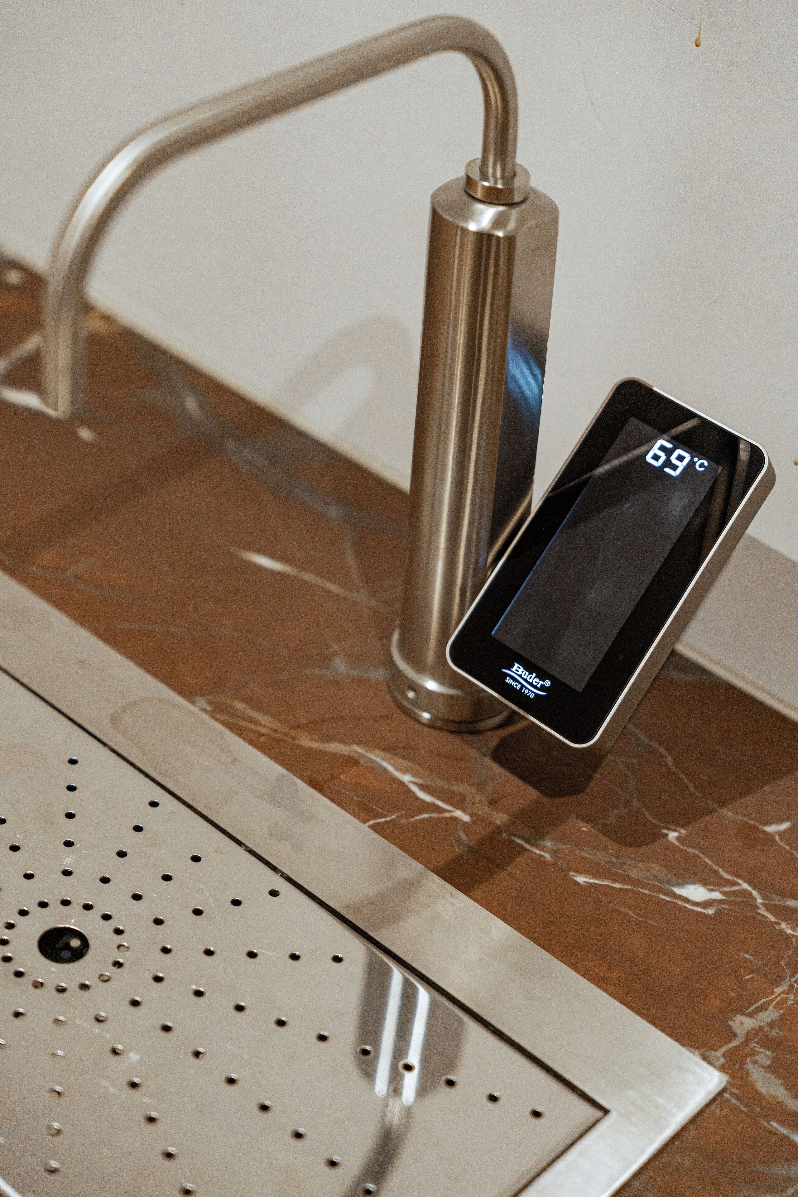 A bathroom with a modern faucet and a digital thermometer displaying 69°C.