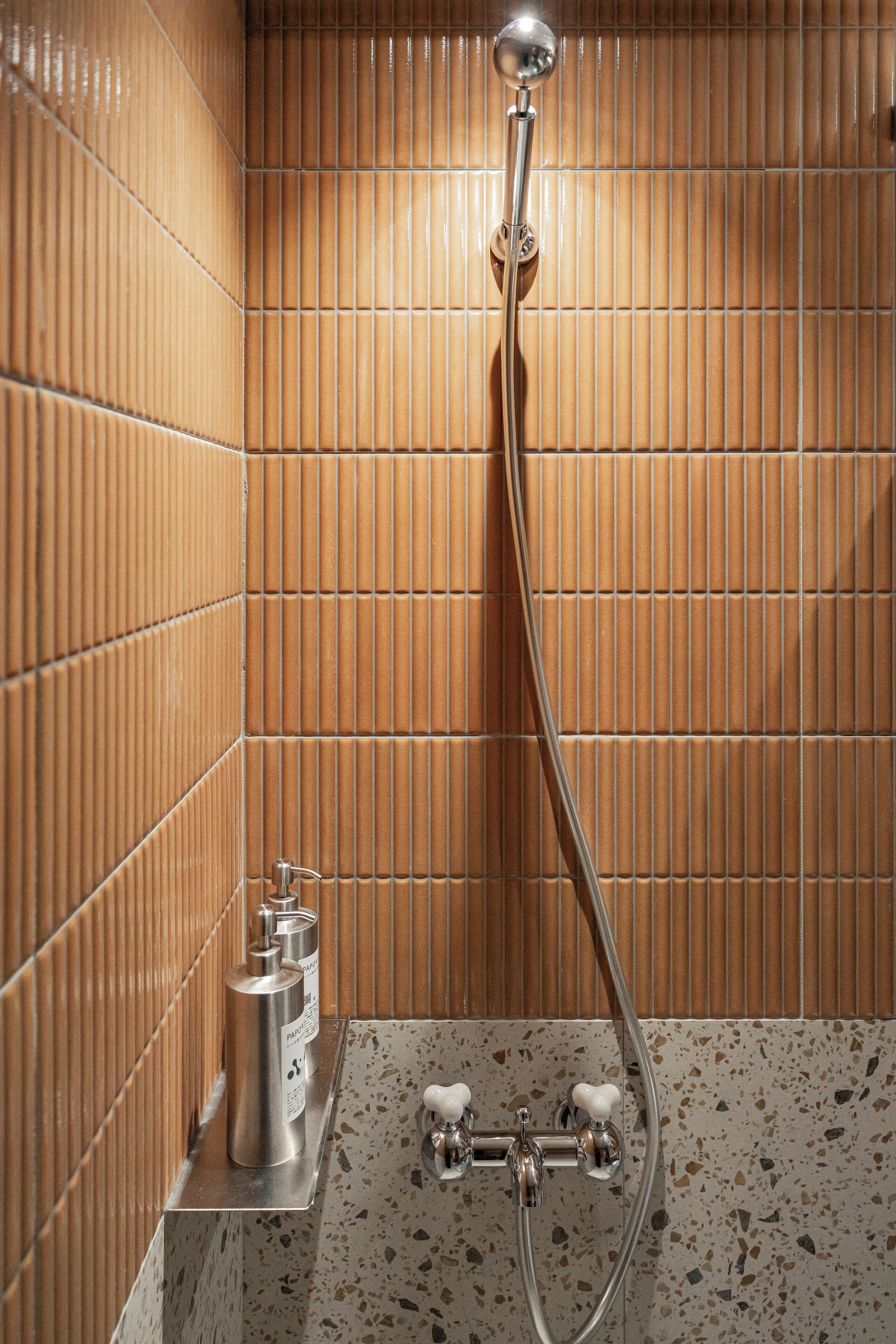 Baño con ducha, paredes de azulejos y lavamanos con grifo.