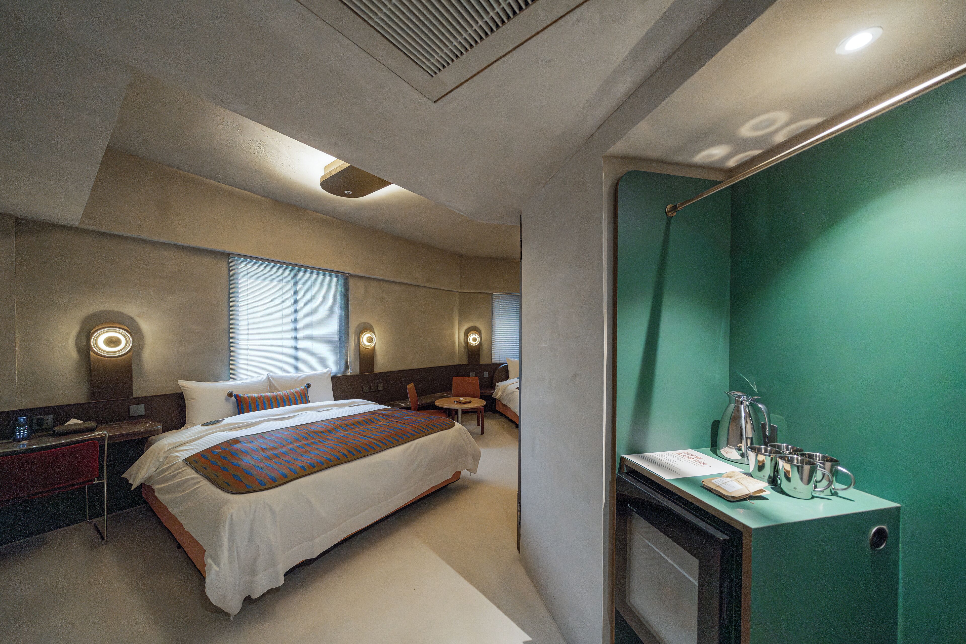 A hotel room with a large bed, a desk, a chair, a small table, and a green wall.