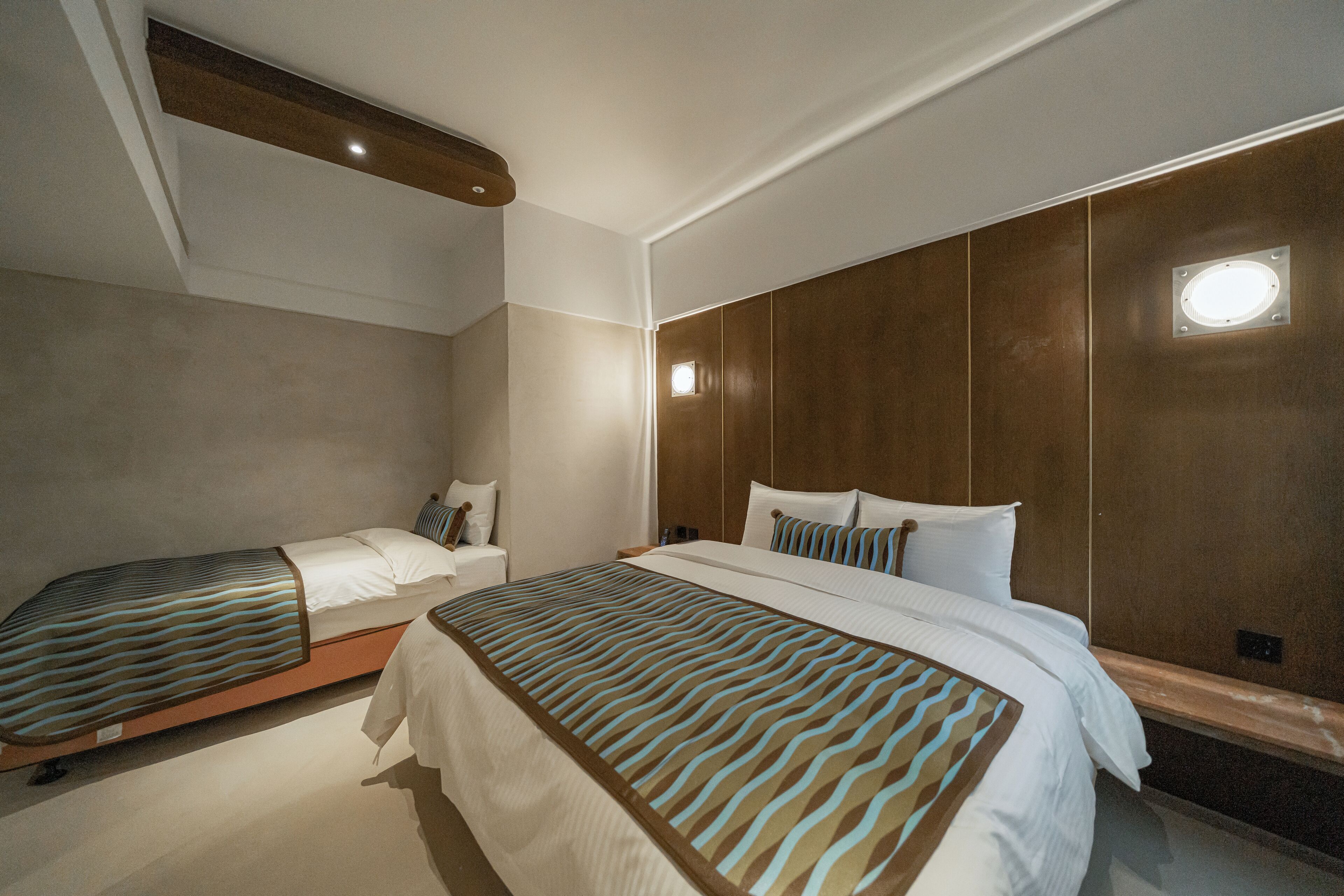 Habitación de hotel con dos camas, cabecera de madera y una ventana pequeña.