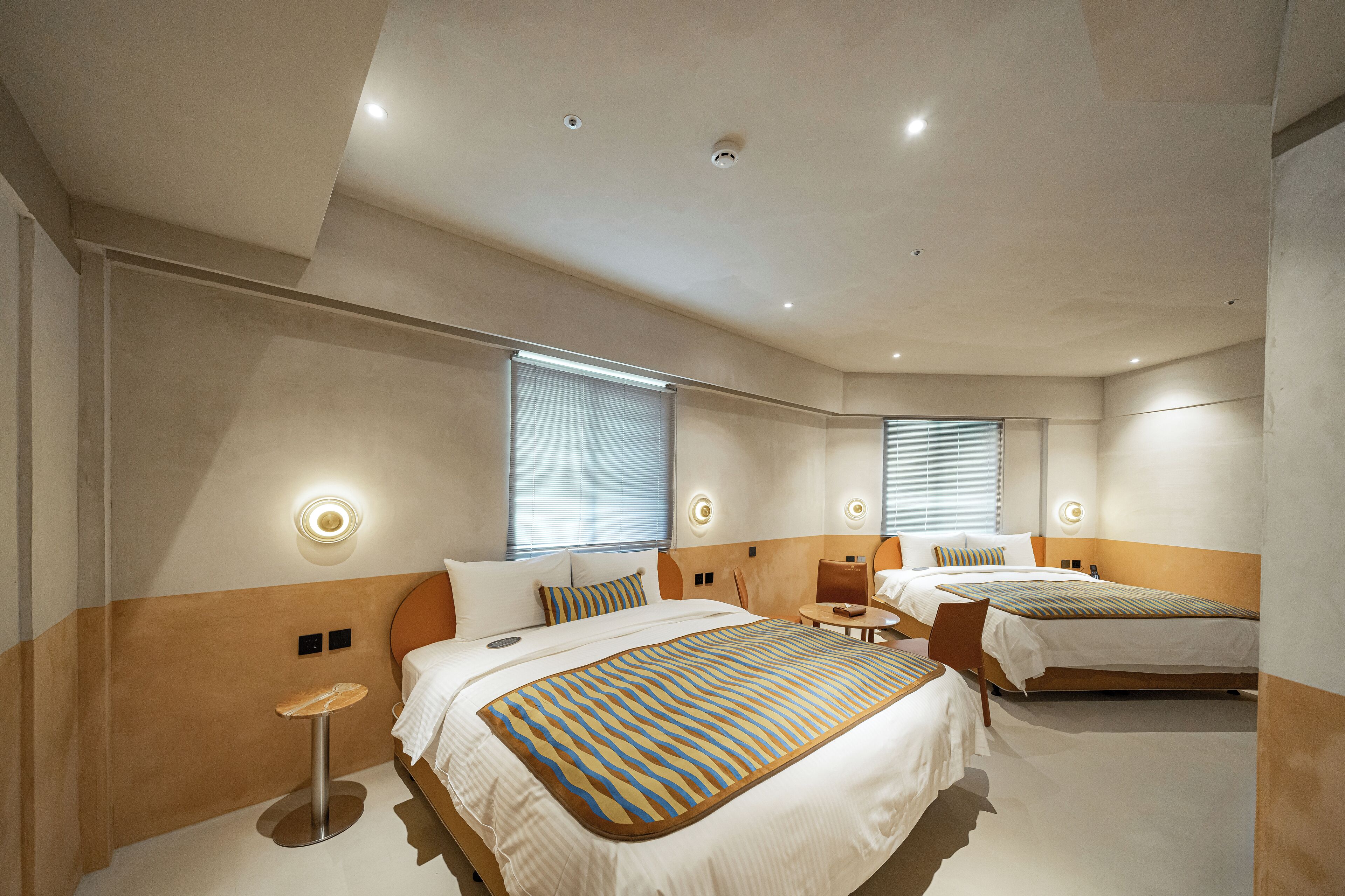 A modern hotel room with a large bed, a smaller bed, a desk, and a chair.