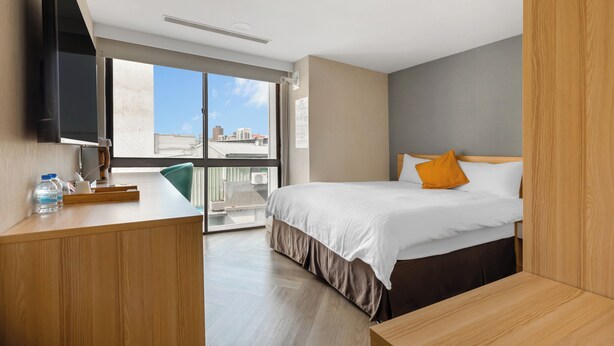 Una habitación de hotel moderna con cama, escritorio, televisión y un amplio ventanal con vistas a la ciudad.