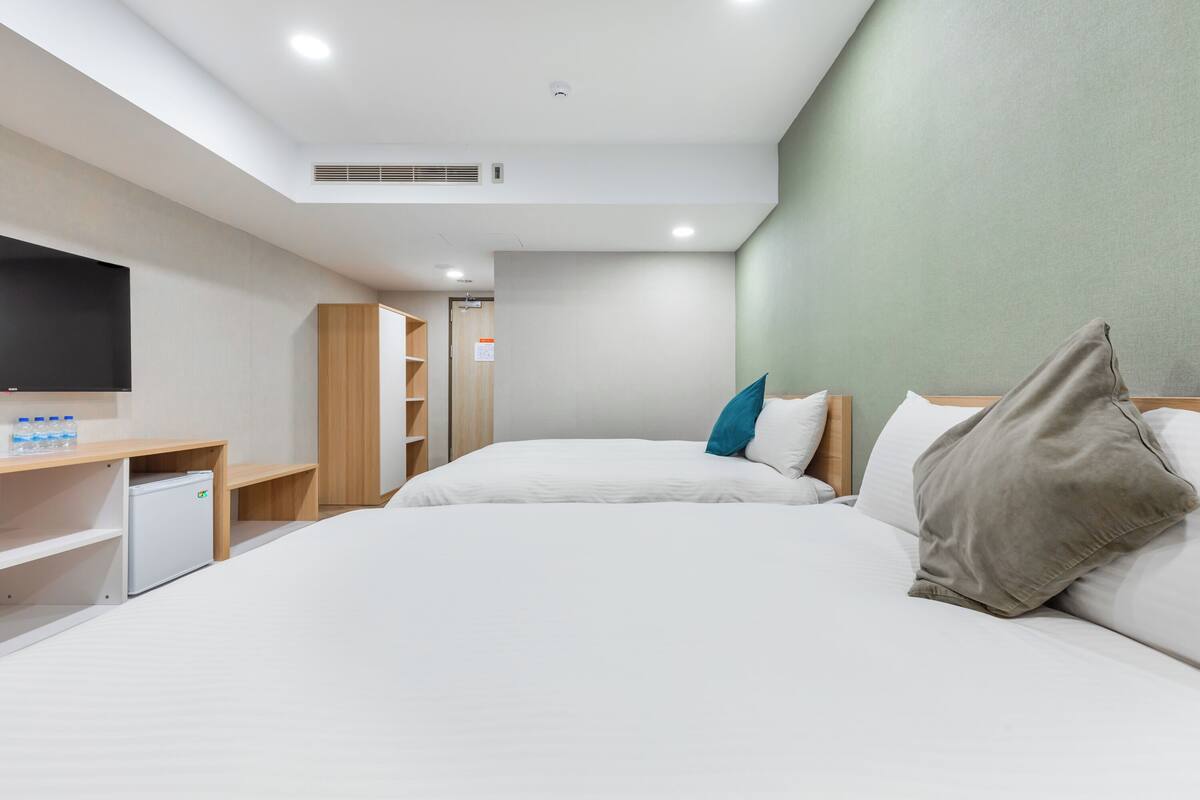 A hotel room with two beds, a TV, a mini-fridge, and a wooden wardrobe.