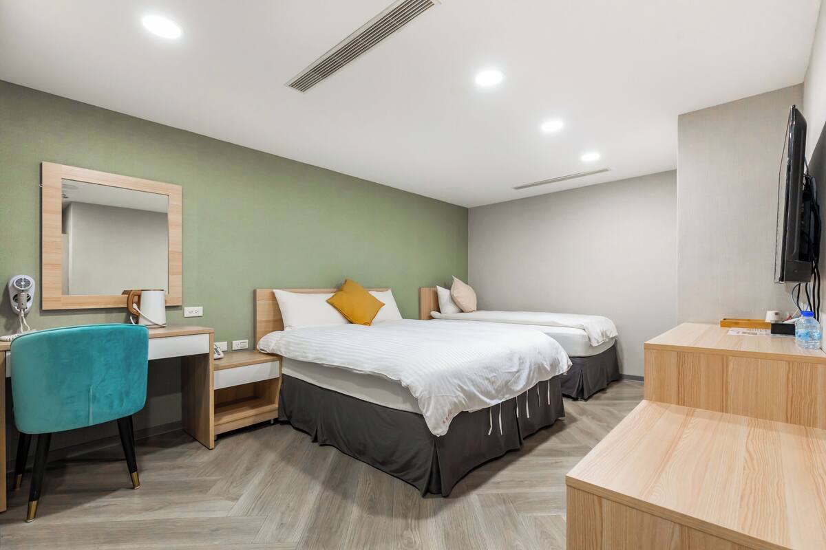 A modern hotel room with two beds, a desk, and a chair.