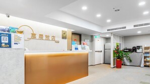 Zona de recepción de un hotel con mostrador, carteles informativos, un refrigerador y una cafetera.