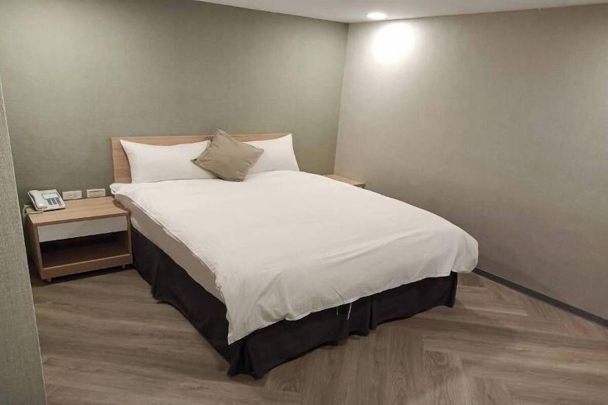 A neatly made bed with a wooden headboard, a bedside table with a lamp, and a phone.