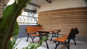 Un espacio al aire libre con bancos y mesas de madera, una planta en maceta y una barandilla de metal.