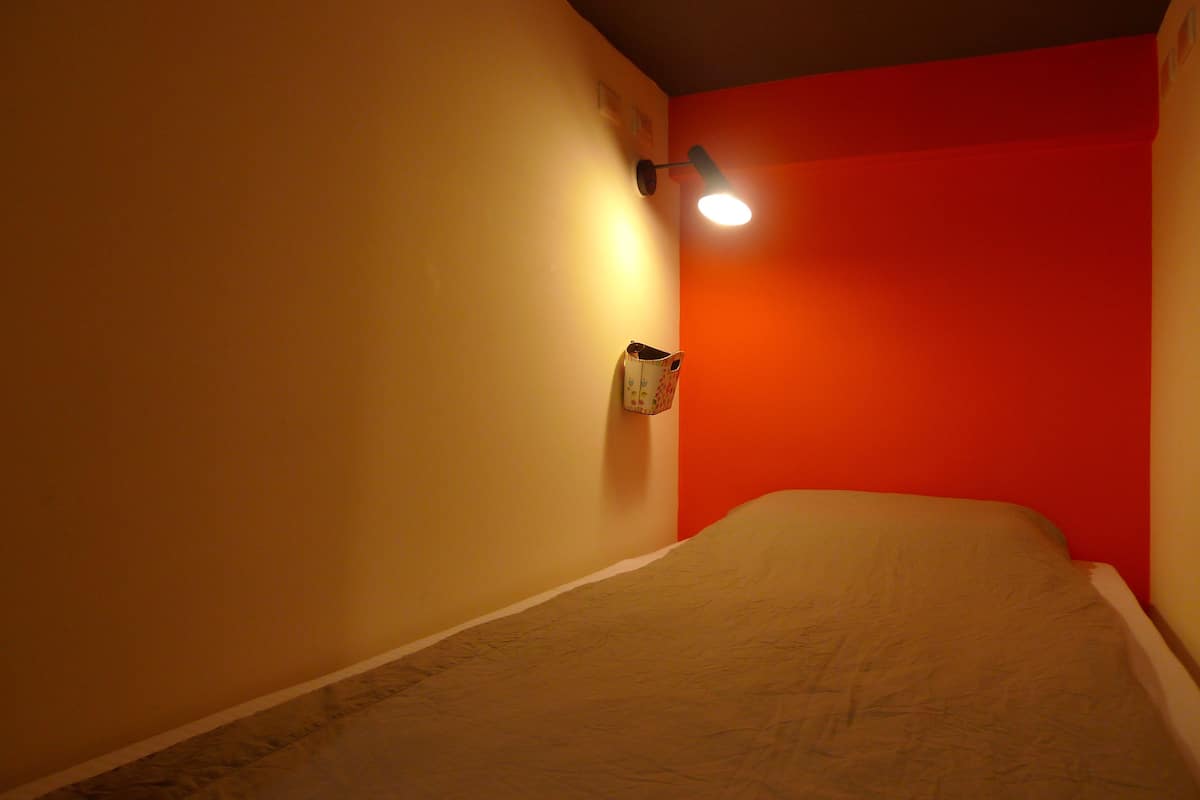 A room with a bed, a wall-mounted light, and a red accent wall.