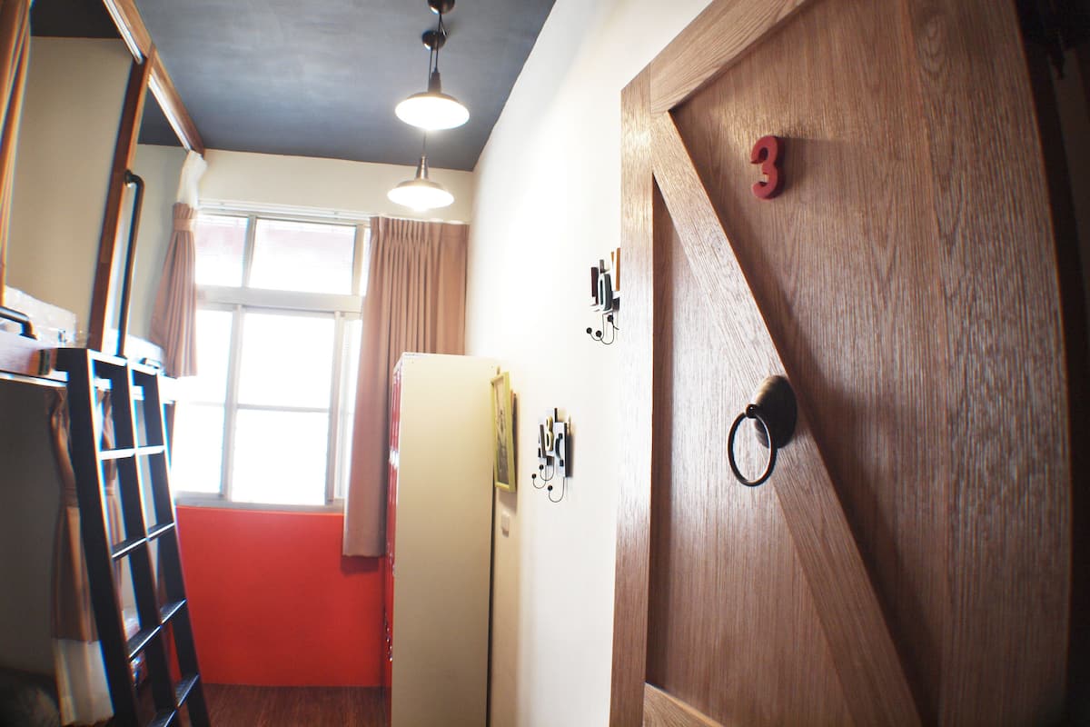 A room with a wooden door, a white wall, and a window with curtains.