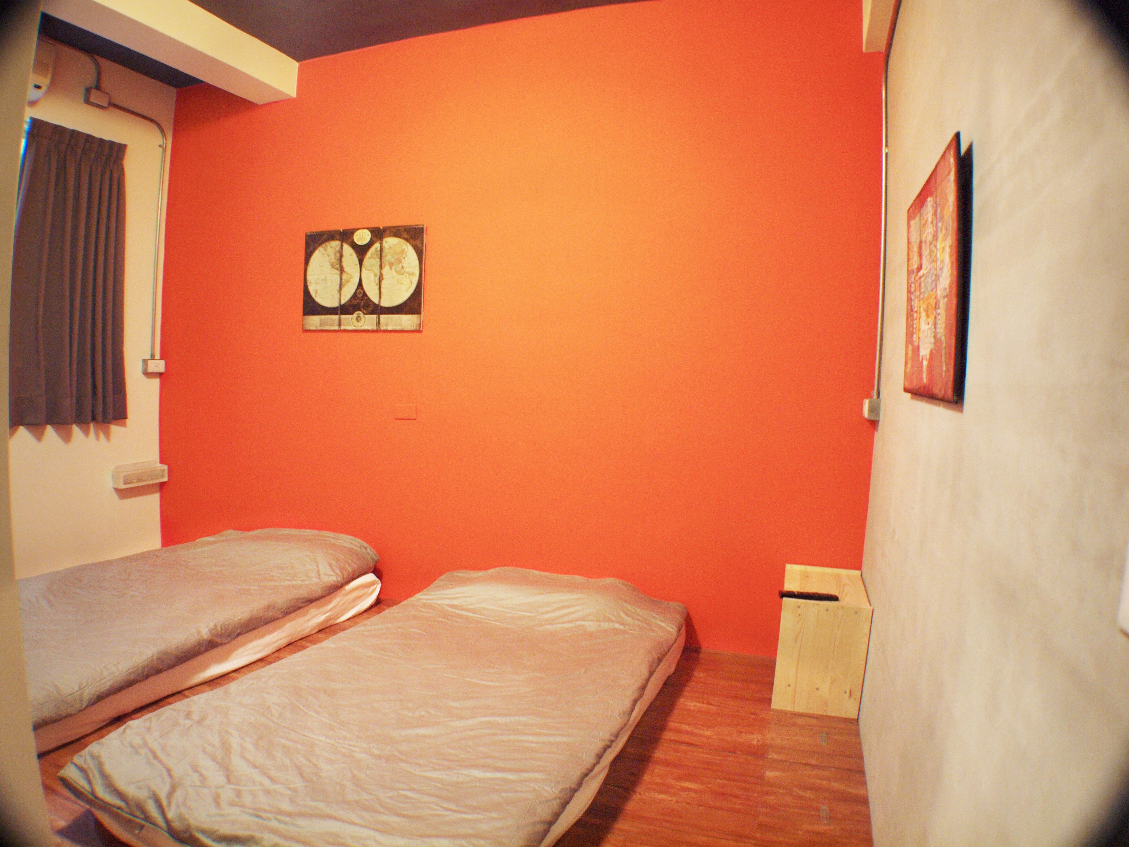 A room with two beds, a small wooden nightstand, a wall-mounted picture, and a window with curtains.