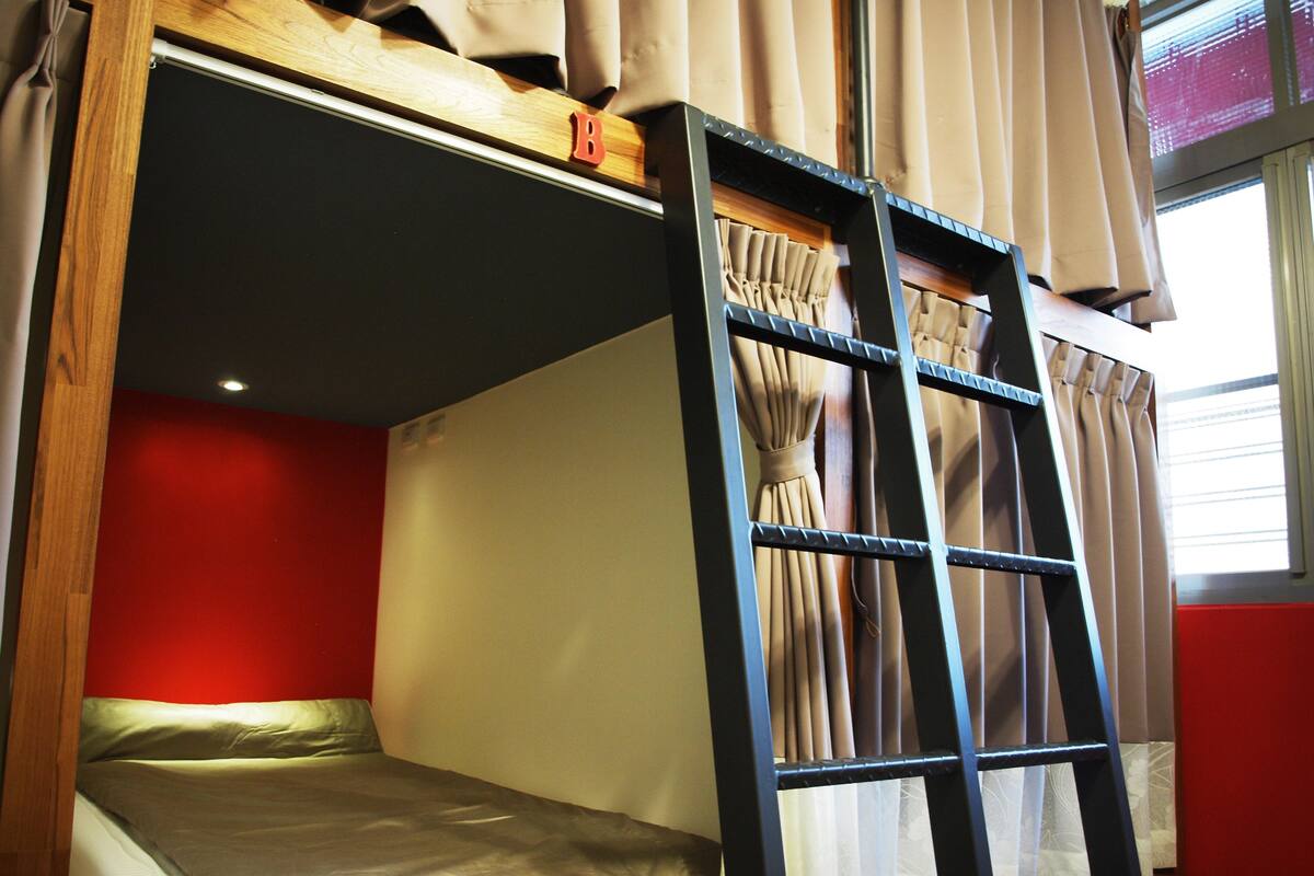 A bunk bed with a ladder, red walls, and curtains.