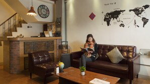 Un rincón de descanso acogedor con un sofá de cuero, una mesa de centro de madera y un globo terráqueo sobre una mesita auxiliar. Un mapa mundial adorna la pared, y un reloj se ve sobre el sofá.