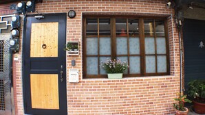 Un edificio de ladrillo con un ventanal grande, una puerta de madera y una maceta pequeña con flores.