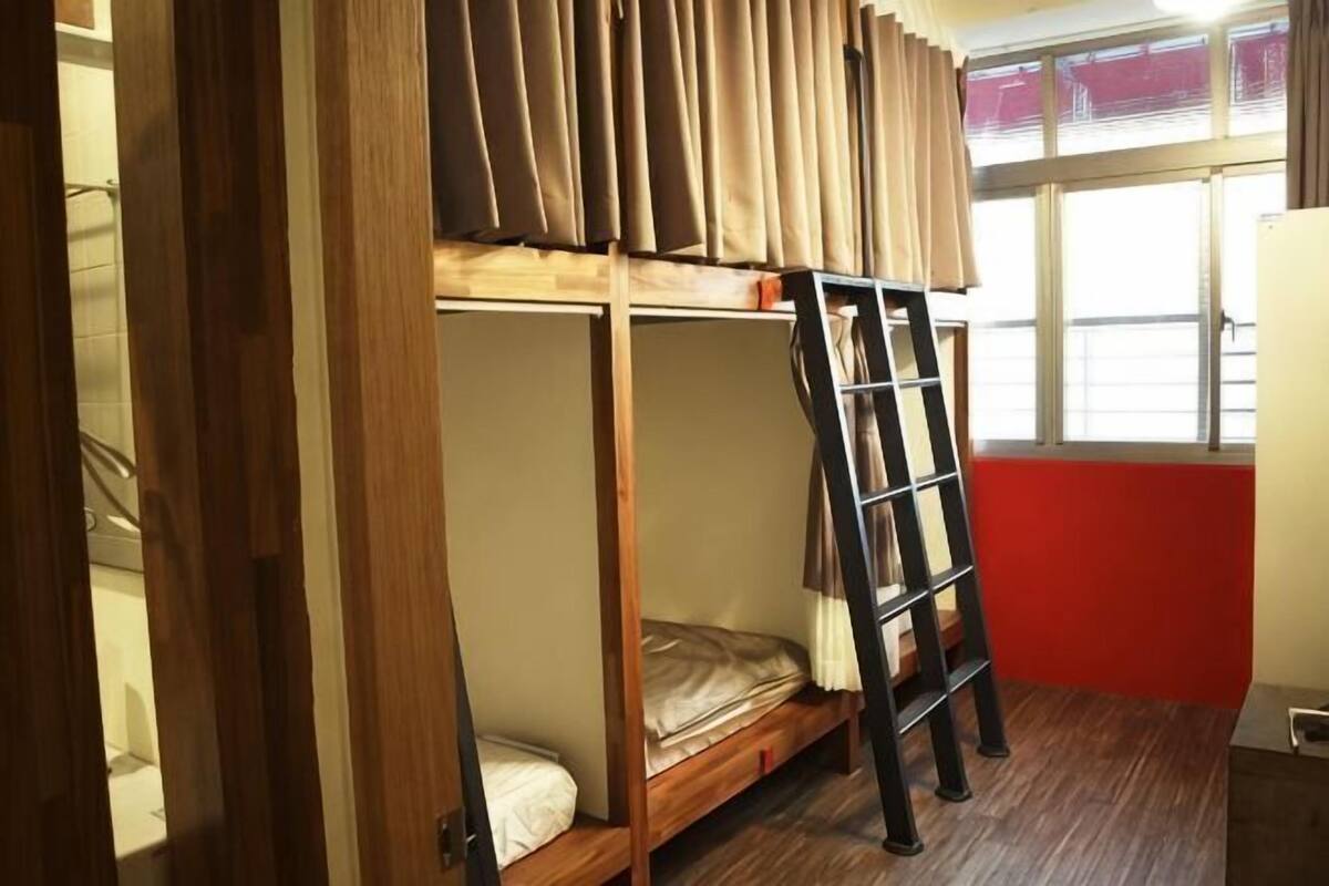 A bunk bed with a ladder, a window with curtains, and a red wall.