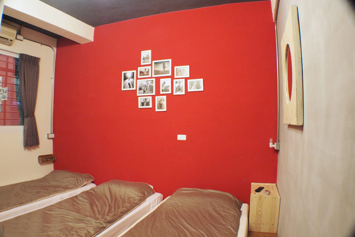 A room with two beds, a red wall, and several photographs displayed.