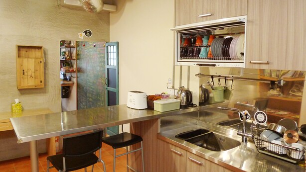 Una cocina con encimera de acero inoxidable, dos taburetes de bar, un refrigerador y un escurreplatos sobre el lavamanos.