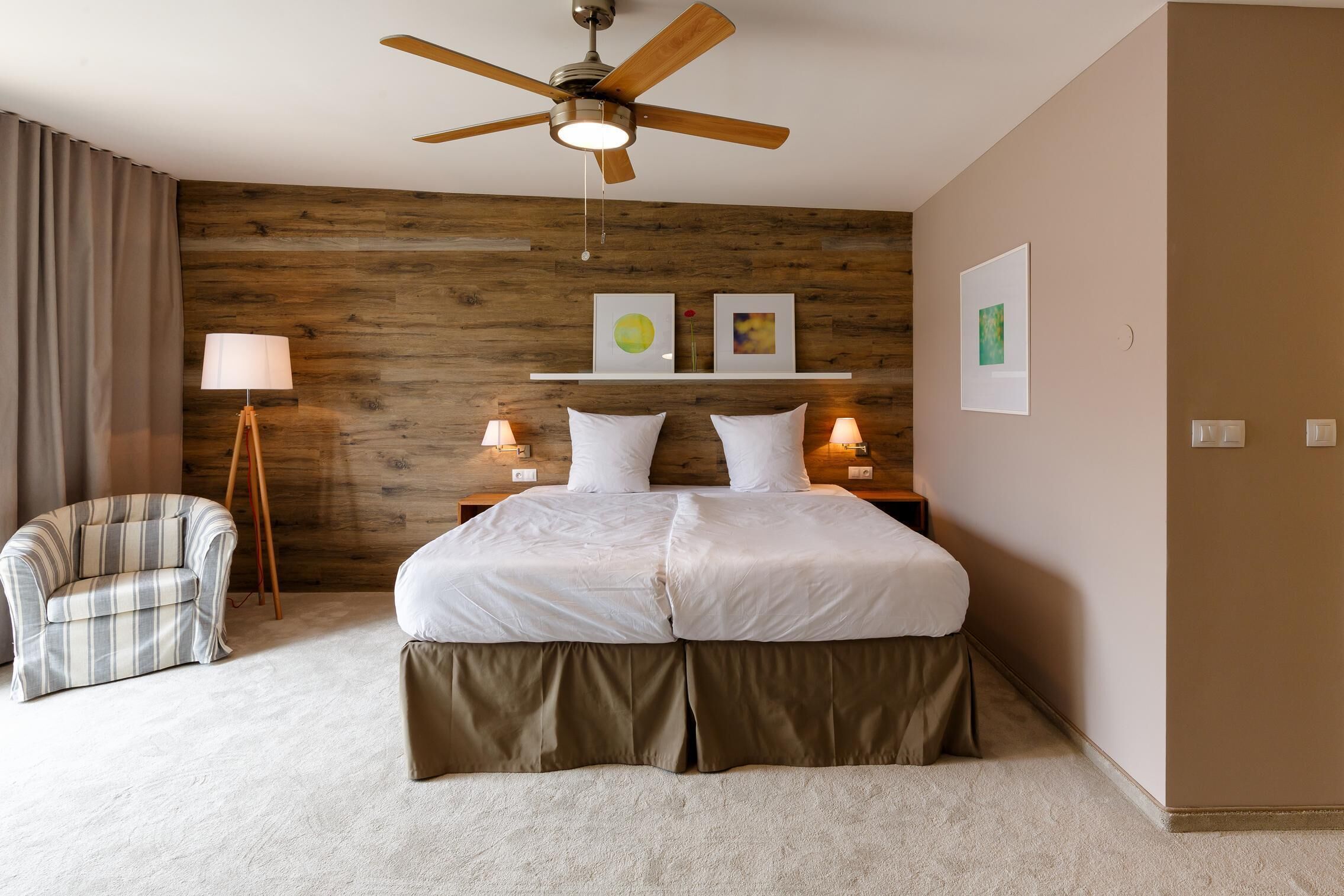 A bedroom with a bed, a standing lamp, a chair, and a ceiling fan.