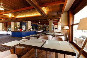 Vestíbulo de hotel con techos de madera, una zona de bar y diferentes arreglos de asientos.