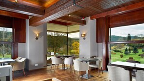 Un espace repas doté d’un plancher en bois, de chaises modernes et de grandes fenêtres offrant une vue sur un paysage verdoyant.