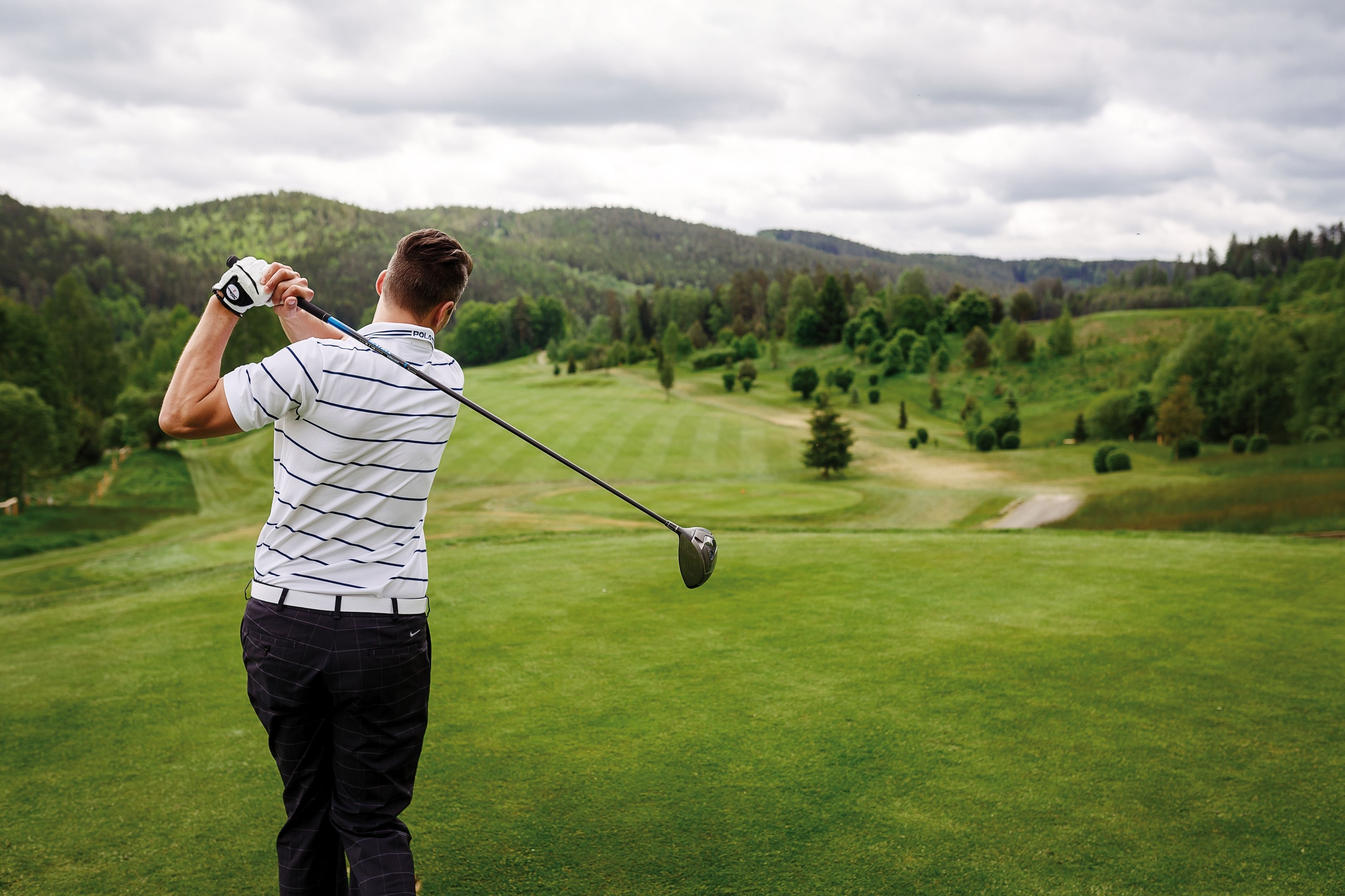 A person playing golf on a well-maintained course with rolling hills and trees in the background.
