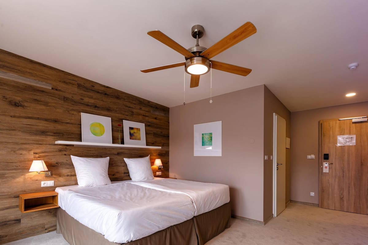 Een slaapkamer met een houten hoofdeinde, een bed met witte beddengoed, een plafondventilator en wandlampen.