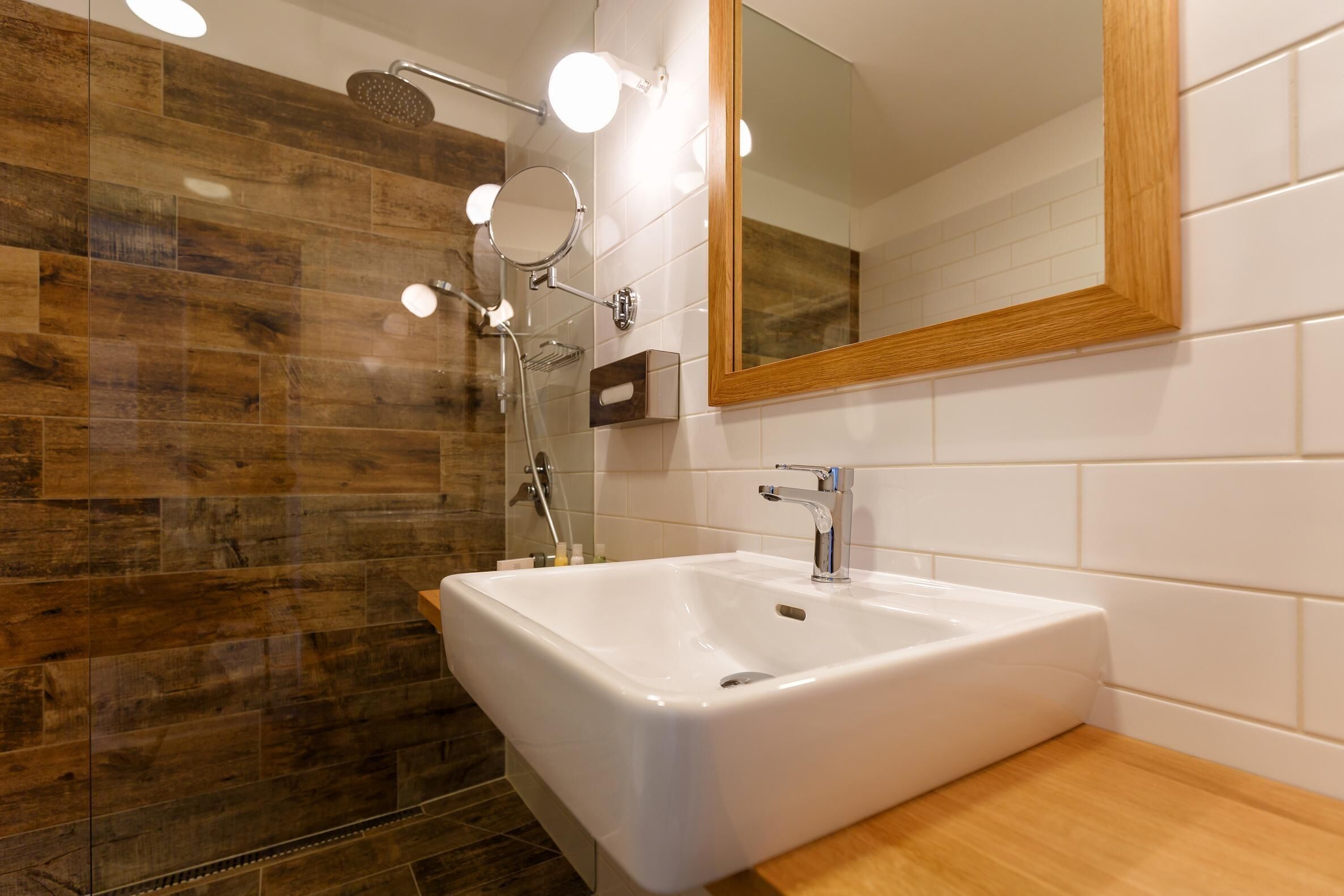 Une salle de bain moderne avec un grand lavabo blanc, un espace de douche en bois et un miroir avec un cadre en bois.