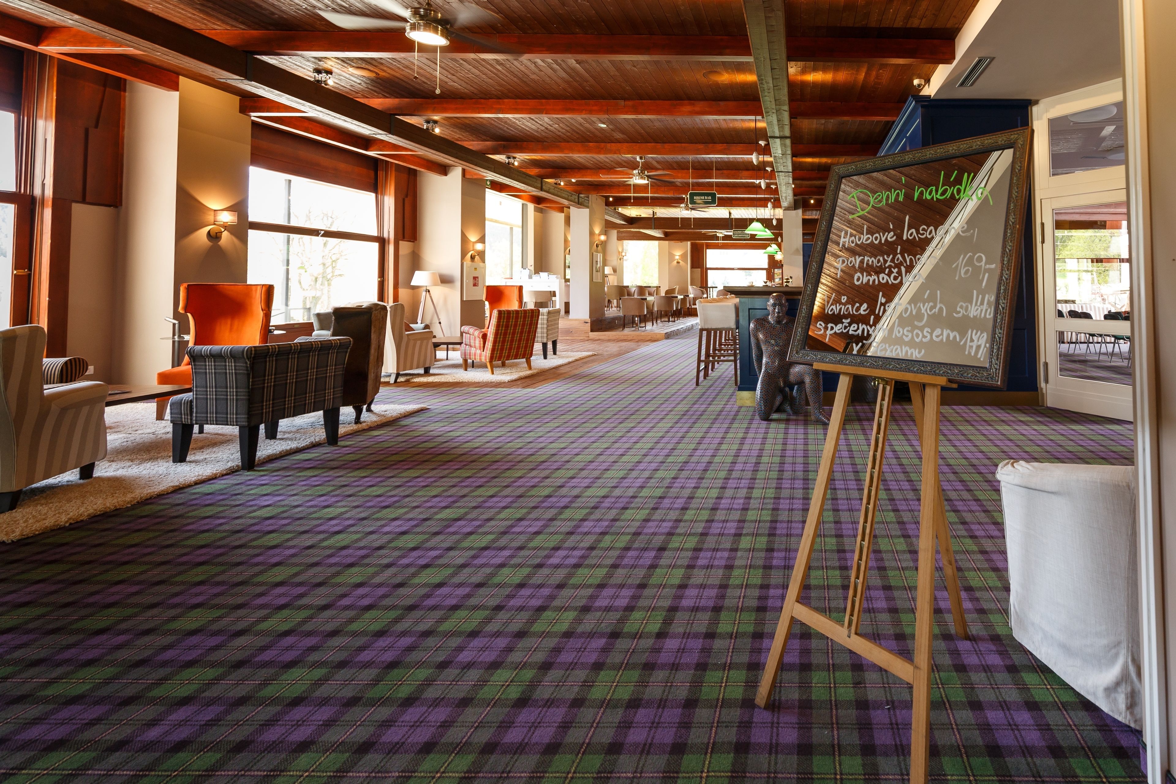 Un vestíbulo amplio con alfombra a cuadros, vigas de madera y un menú en una pizarra.