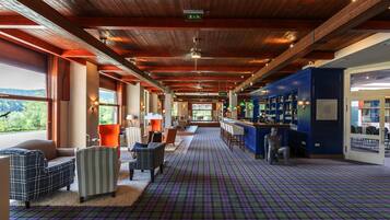 A spacious hallway with a checkered floor, wooden ceiling beams, and a bar area with shelves.