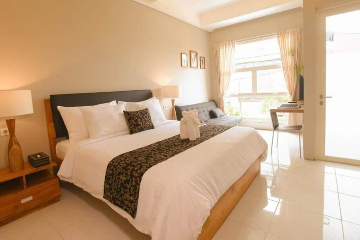 A hotel room with a large bed, bedside tables, a desk, and a window with curtains.