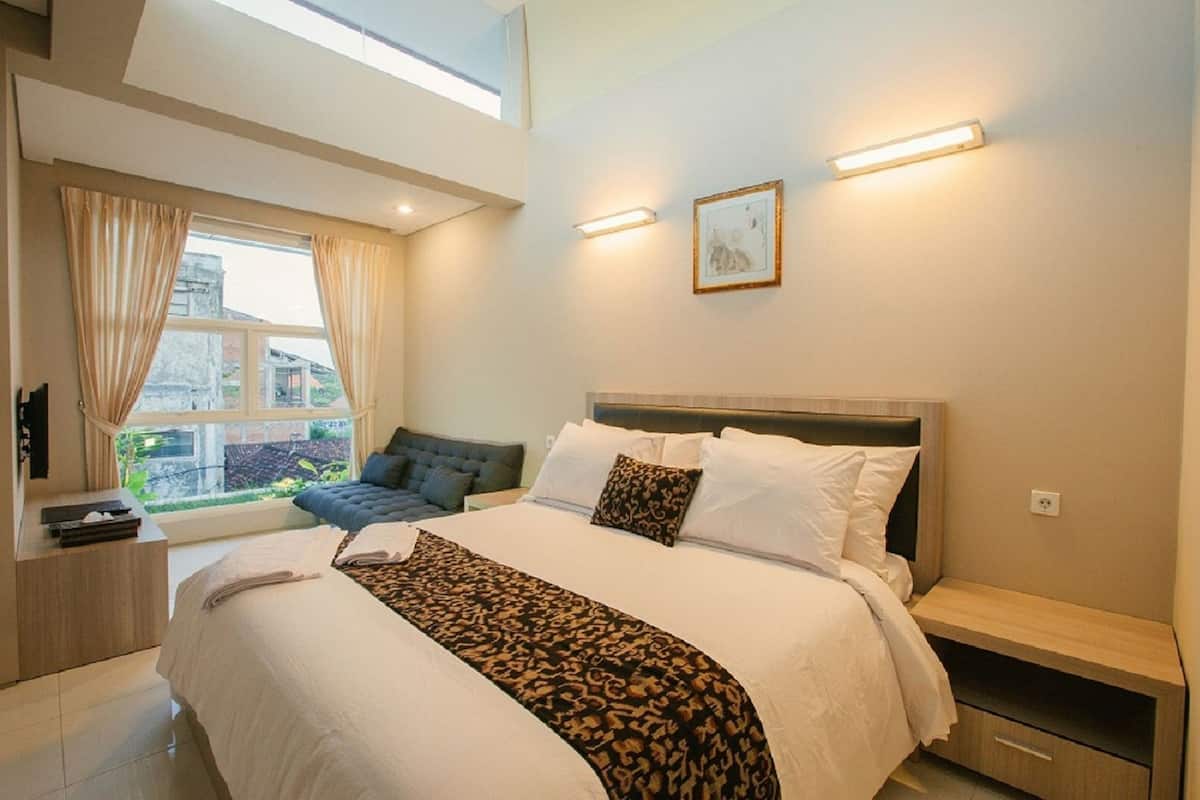 A modern hotel room with a large bed, a sofa, a desk, and a window with curtains.
