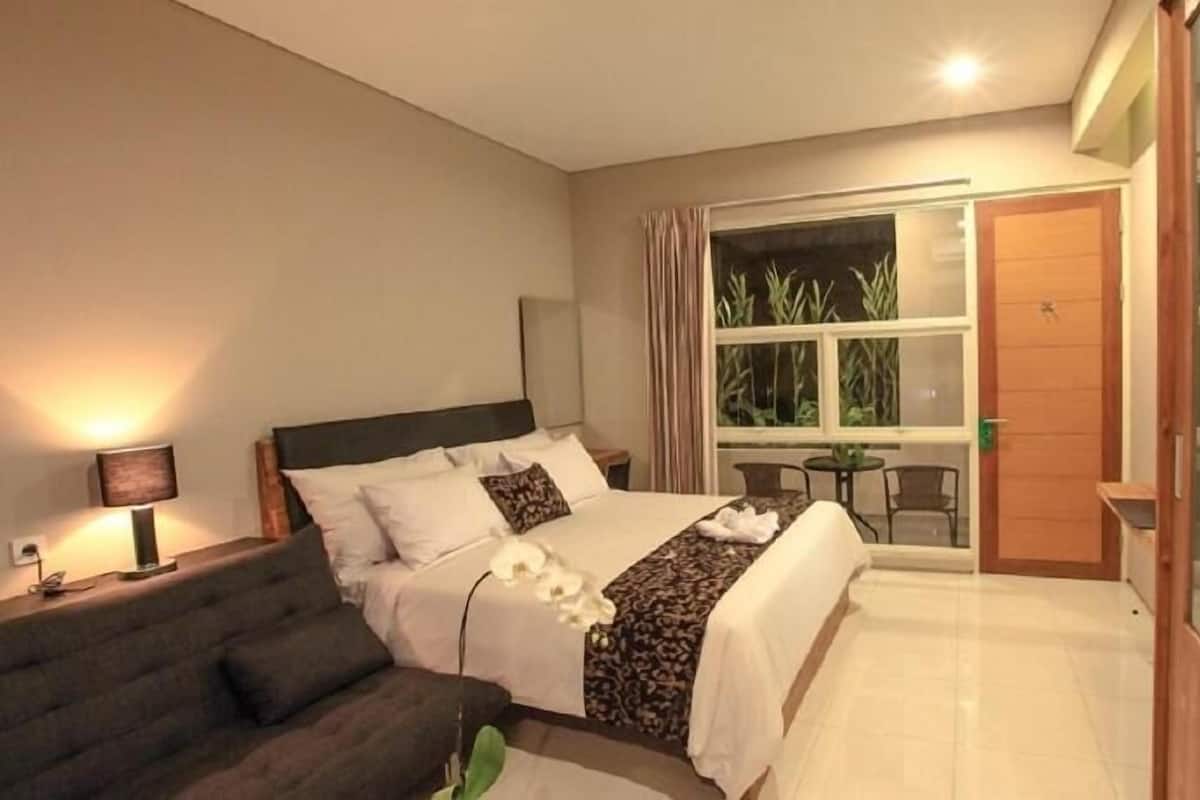 A hotel room with a bed, a sofa, a desk with a lamp, a window with curtains, and a sliding door.