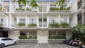 A multi-story residential building with balconies, a parking area, and a car parked in front. - Bali True Living Apartment (Denpasar)