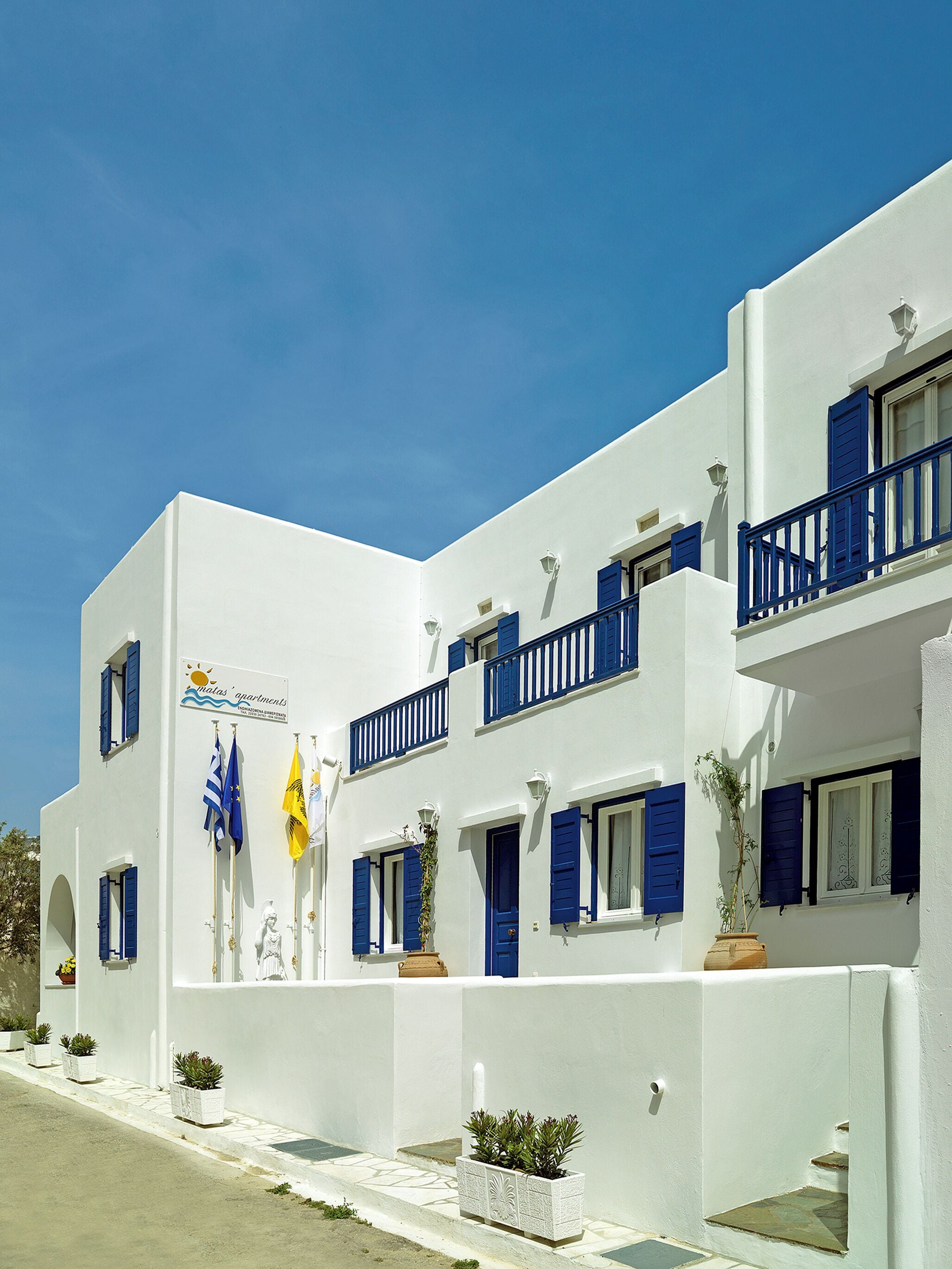 A white building with blue shutters and balconies, featuring a sign for 'Malus Apartments'.