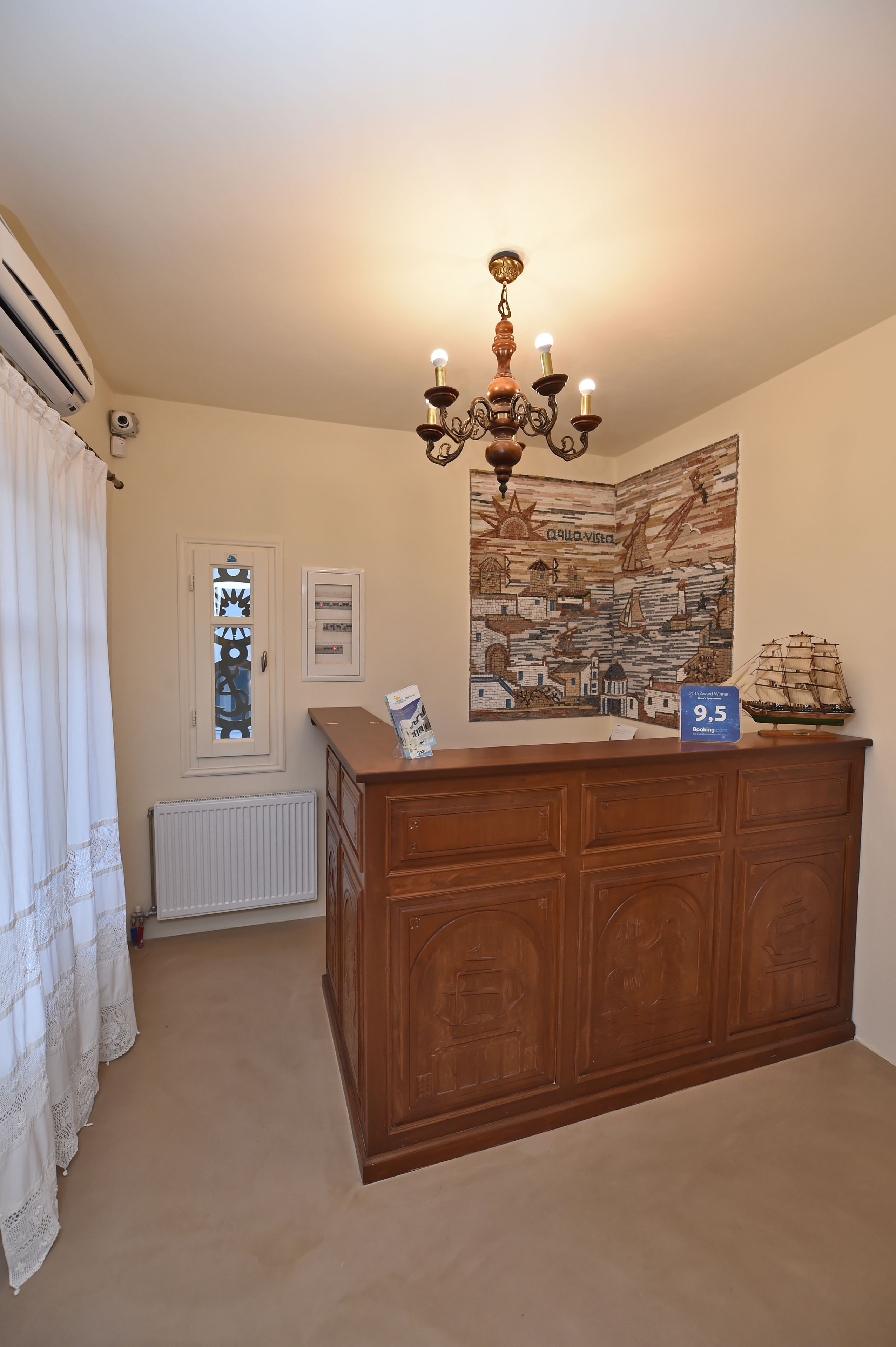 A room with a wooden reception desk, a chandelier, a window with a curtain, a radiator, and a wall with a map and a ship model.